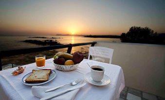a table with a plate of food , bread , fruit , and a cup of coffee on an outdoor balcony overlooking the ocean at sunset at Sea Breeze
