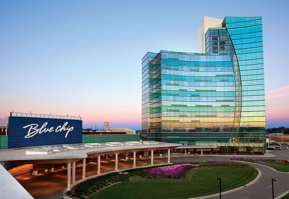 a large blue building with a glass exterior is surrounded by a curved blue sign and greenery at Blue Chip Casino Hotel and Spa