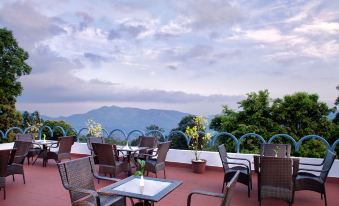 a patio with a view of mountains and a pool , surrounded by chairs and tables at Sterling Munnar