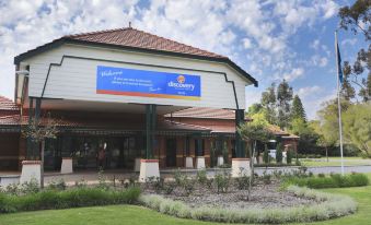 a large white building with a blue sign and a grassy area in front of it at Discovery Parks - Perth Airport