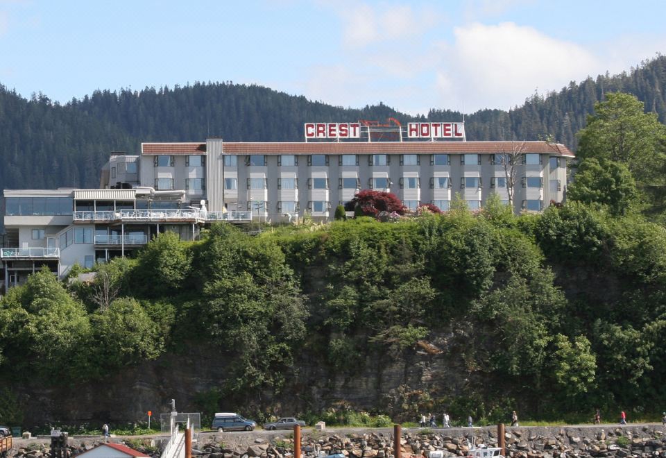 a large hotel situated on top of a hill overlooking a body of water , surrounded by trees at Crest Hotel