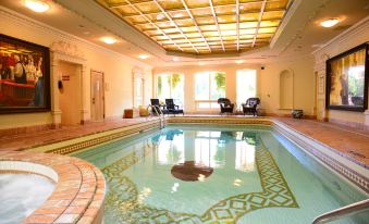 a large , empty indoor swimming pool with a gold - colored trim and blue tiles , surrounded by lounge chairs and windows at Prince of Wales