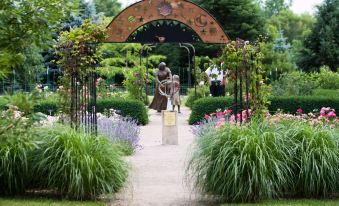 a beautiful garden with a statue of a person and an archway entrance , surrounded by lush greenery and vibrant flowers at Courtyard Toledo Airport Holland