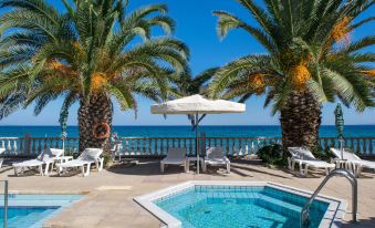 a pool surrounded by palm trees and a view of the ocean , with lounge chairs and umbrellas placed around the area at Paradise Beach Hotel