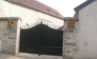 a black wrought iron gate is set in a stone wall with a building behind it at Le 5