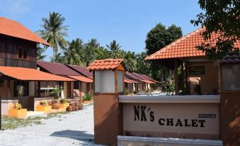 a sign for nk 's chalet is in front of a tropical resort with orange buildings at Nks Chalet