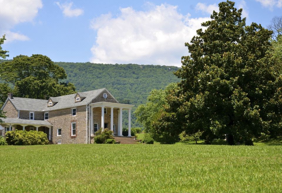 a large house with a porch and columns is surrounded by green grass and trees at Mountain Cove Farms Resort