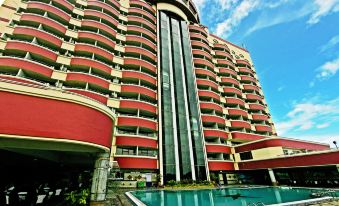 a tall building with a red facade and many windows is reflected in the pool at Planet Holiday Hotel & Residence