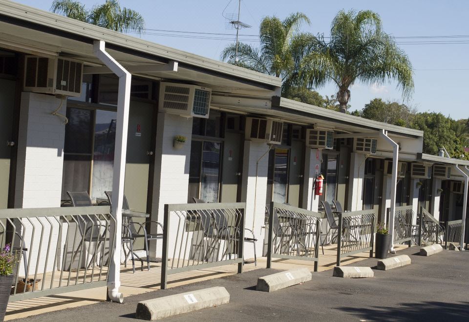 a row of small , white houses with metal railings and palm trees in the background at Gatton Motel