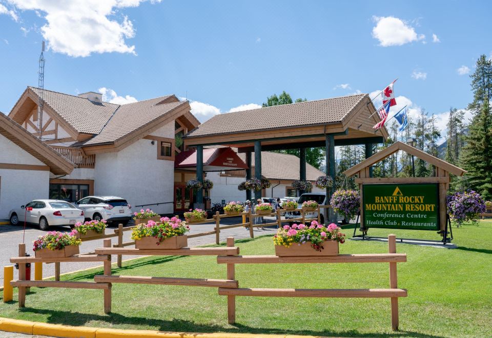a large building with a covered entrance and flower boxes in front , surrounded by green grass at Banff Rocky Mountain Resort