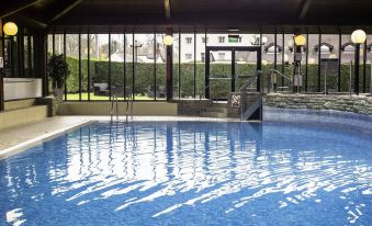 a large indoor swimming pool surrounded by glass walls , with several people enjoying their time in the water at Airport Inn Manchester