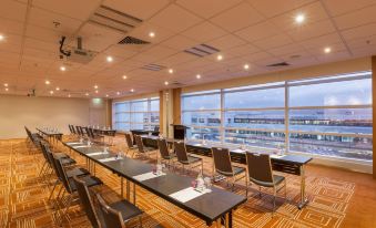a conference room with rows of tables and chairs , large windows , and a city view at PARKROYAL Melbourne Airport