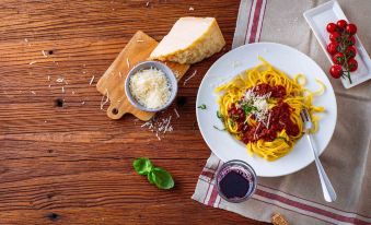 a plate of pasta with a sauce , cheese , and basil on a wooden table , accompanied by a wine glass and a bowl of sauce at Ibis Como