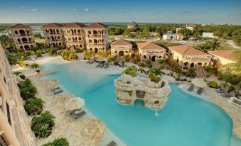 a large resort with a pool and water features is surrounded by buildings , including one with a rocky structure at Coco Beach Resort