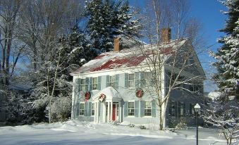 a snow - covered house with a red roof and white trim , surrounded by trees and snow at Centennial House
