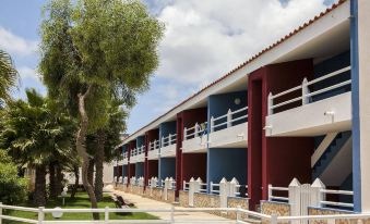 a row of multi - story buildings with red and blue roofs , surrounded by green grass and trees at Murdeira Village Resort