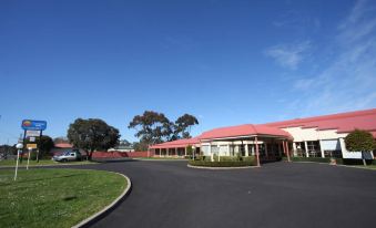 a large building with a red roof is surrounded by trees and grass , under a clear blue sky at Grange Burn Motel