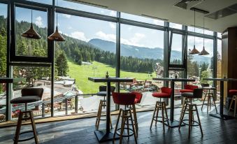 a modern , open - air restaurant with red bar stools and tables , offering a view of the surrounding mountains at Rila Hotel Borovets