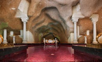 a modern , cave - like structure with a red and white interior , surrounded by marble columns and a red floor at Sacred House