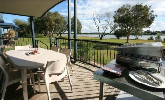 a wooden deck overlooking a body of water , with a dining table and chairs set up for a meal at Discovery Parks - Ballina