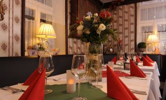 a table is set with red napkins , wine glasses , and a vase of flowers in the center at Hotel Berg