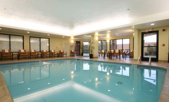 a large swimming pool is surrounded by tables and chairs in a room with yellow walls at Courtyard Flint Grand Blanc