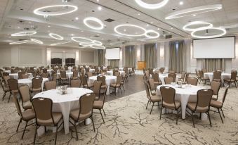 a large , well - lit banquet hall filled with round tables and chairs , ready for a formal event at Crowne Plaza Kitchener-Waterloo