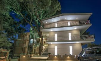 a modern building with a staircase and large windows , surrounded by trees and lit up at night at Koukounaria Hotel & Suites