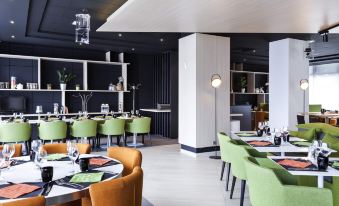 a modern restaurant with green and orange chairs , a black ceiling , and white shelves filled with items at Novotel Tours Centre Gare