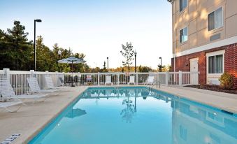 an outdoor swimming pool surrounded by a hotel , with several lounge chairs and umbrellas placed around the pool area at Homewood Suites by Hilton Olmsted Village (Near Pinehurst, NC)