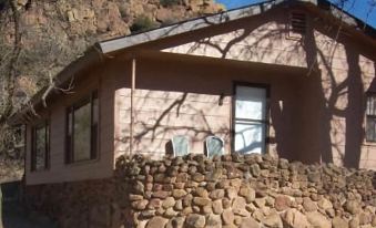 a small , pink house with a stone foundation and window is surrounded by rocks and trees at Quartz Mountain Resort