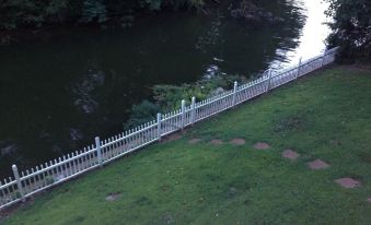 a white picket fence is lining a grassy area next to a river , with trees in the background at The Waterford