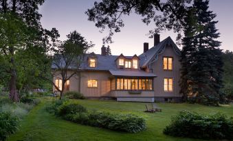 a large , two - story house surrounded by trees and grass , with a paved walkway leading up to the front door at Gothic Eves Inn and Spa Bed and Breakfast