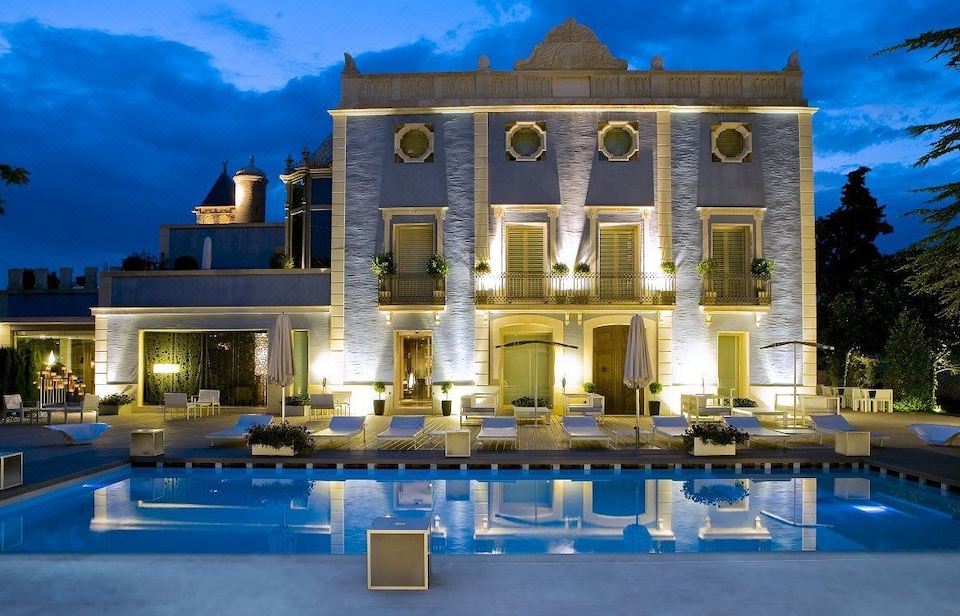 a large villa with a swimming pool in front of it , illuminated by lights at night at Hotel Ferrero