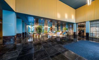 a modern , well - lit lobby with blue and gold walls , black marble flooring , and various seating options at NH Collection Antwerp Centre
