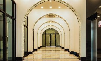 a long , white - tiled hallway with black and white checkered flooring , leading to a room with arched windows at Alfahad Hotel