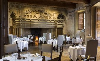 a large , ornate dining room with multiple tables set for a formal dinner , surrounded by chairs and a fireplace at Chateau de Bagnols