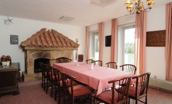 a large dining table with pink tablecloth and chairs in a room with a fireplace at Dronninglund Hotel