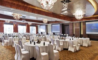 a large banquet hall with white tables and chairs , chandeliers hanging from the ceiling , and a red carpet at Novotel Mumbai Juhu Beach