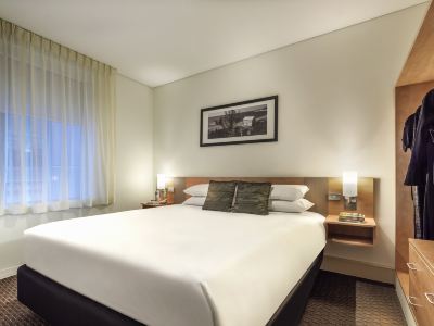 a large bed with white sheets and pillows is in a hotel room with a window at Ibis Melbourne Hotel and Apartments