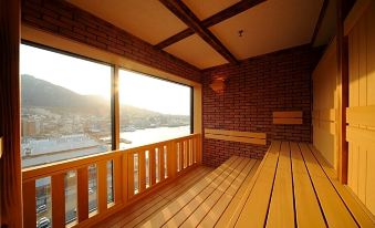 a room with a wooden floor and brick walls , featuring a large window overlooking a body of water at La Vista Hakodate Bay