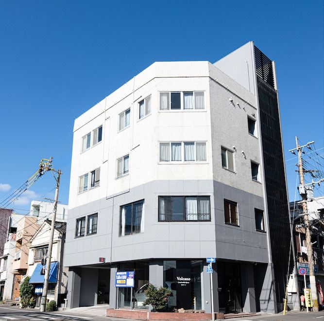 a city street with a white and gray building on the corner , surrounded by other buildings at Volcano