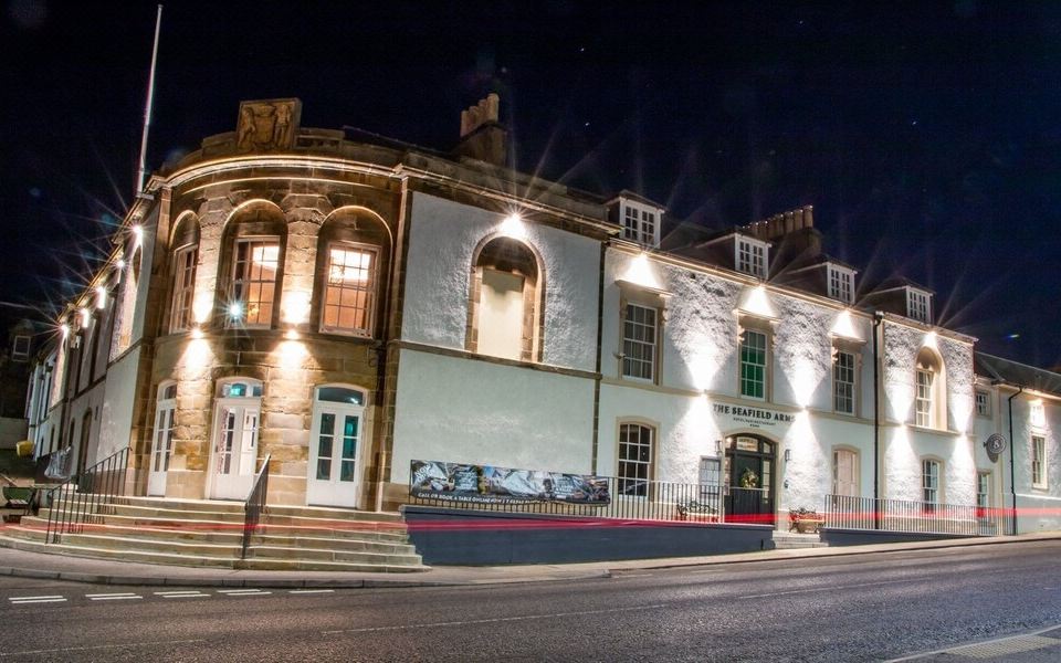 a large , white building with multiple windows and balconies , lit up at night , situated on the side of a street at The Seafield Arms-Cullen