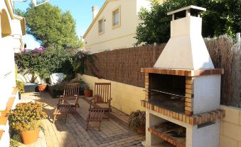 a brick patio with a barbecue grill , chairs , and a brick chimney is surrounded by potted plants at Sally