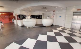 a modern office lobby with two white reception desks and a black and white checkered floor at Idea Hotel Milano Malpensa Airport