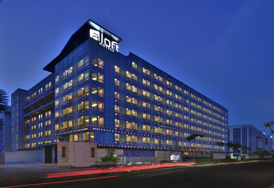 a large building with many windows and a blue sky in the background , as well as a car driving down the street at Aloft New Delhi Aerocity