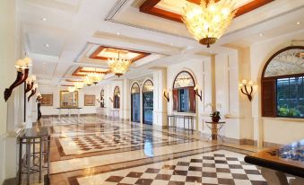 a grand , ornate hotel lobby with white walls , gold accents , and a checkered floor is illuminated by multiple chandeliers at Melia Purosani Yogyakarta