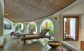a large , curved room with several wooden lounge chairs and a stone floor is adorned with potted plants at Tabacón Thermal Resort & Spa