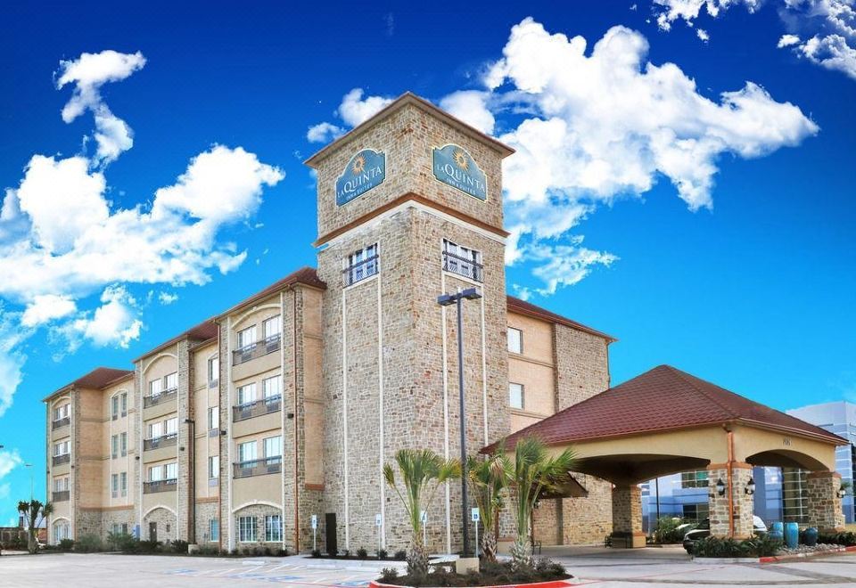 a large hotel building with a clock tower , surrounded by palm trees and a parking lot at La Quinta Inn & Suites by Wyndham Dallas Grand Prairie South