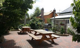 a brick patio with two picnic tables , one on the left and one on the right , surrounded by greenery at Westbury Gingerbread Cottages